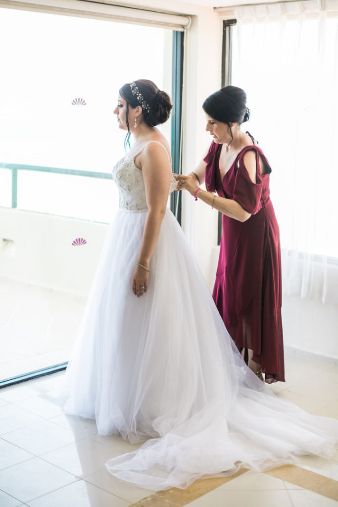 Bride waits as mother fastens the back of her dress