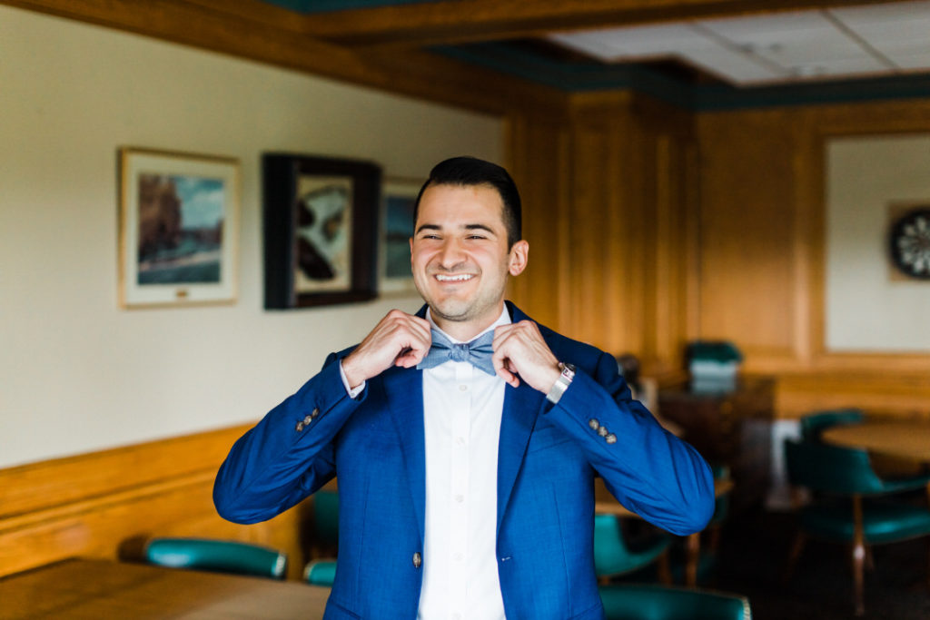 Groom smiles as he adjusts his light blue bow tie