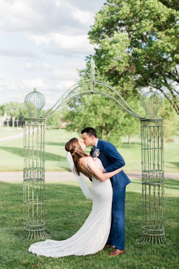Bride and groom kiss under the archway of their outdoor summer Edgewood Club wedding ceremony