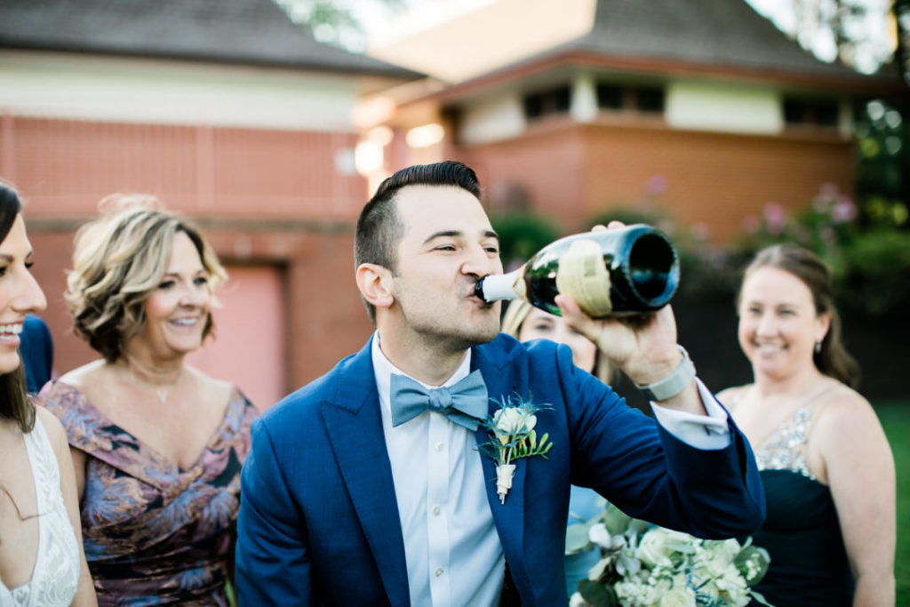 Groom drinks from bottle of champagne