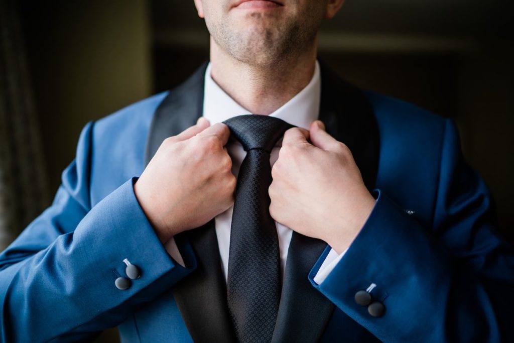 Groom adjusts the collar of his shirt as he gets ready for his wedding