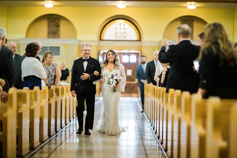 Bride smiles as father walks her down the aisle