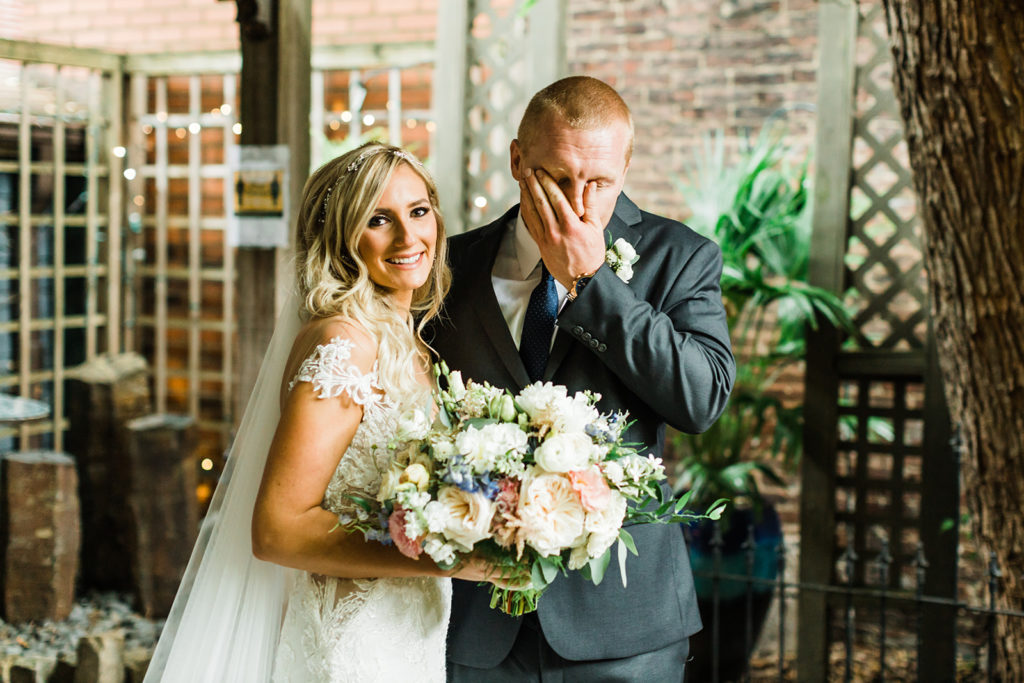 Groom wipes tears from his eyes as bride smiles at the camera