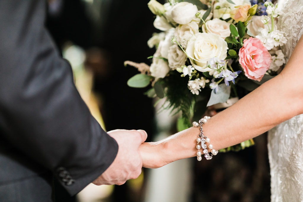 Macro photo of bride and groom holding hands during ceremony