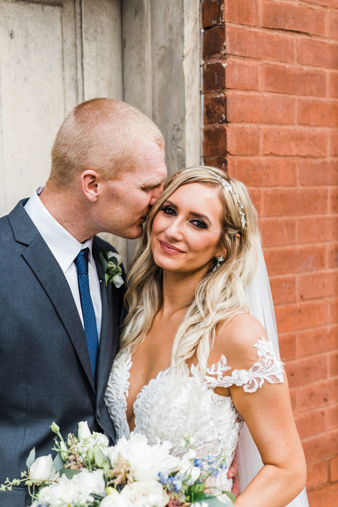 Groom nuzzles brides head as she smiles into the camera