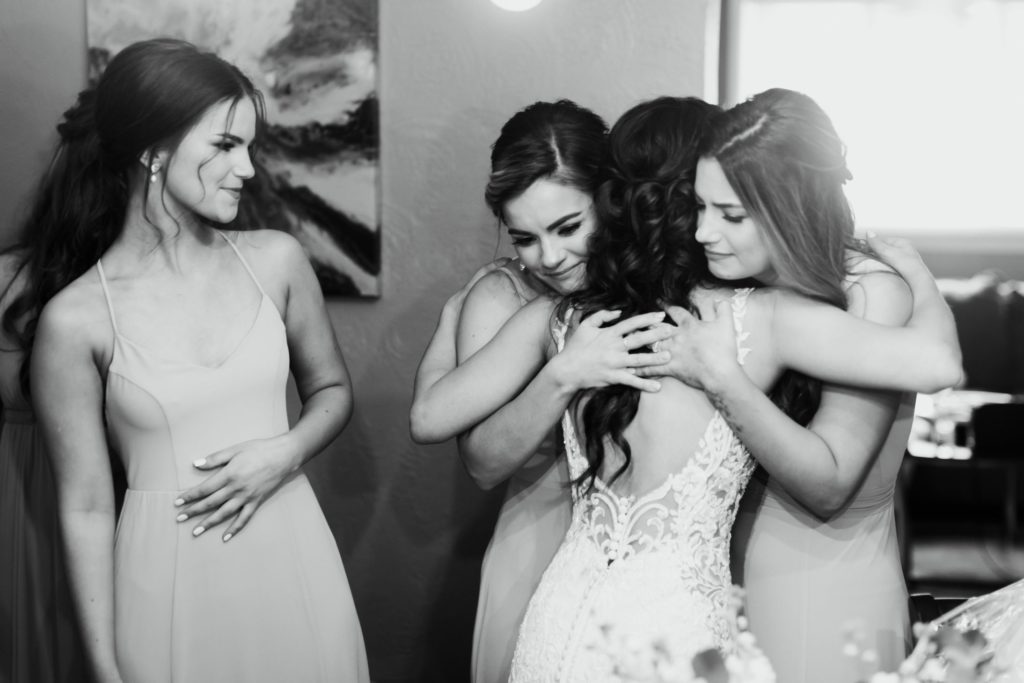 Bride hugs two bridesmaids as one looks on smiling
