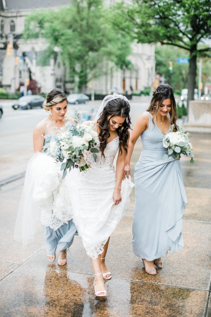 Bridesmaids assist bride with her train on her dress as they walk