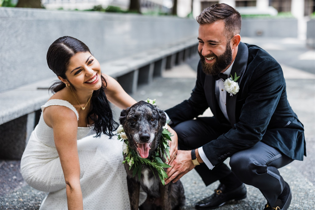 Bride and groom petting their flower dog and smiling