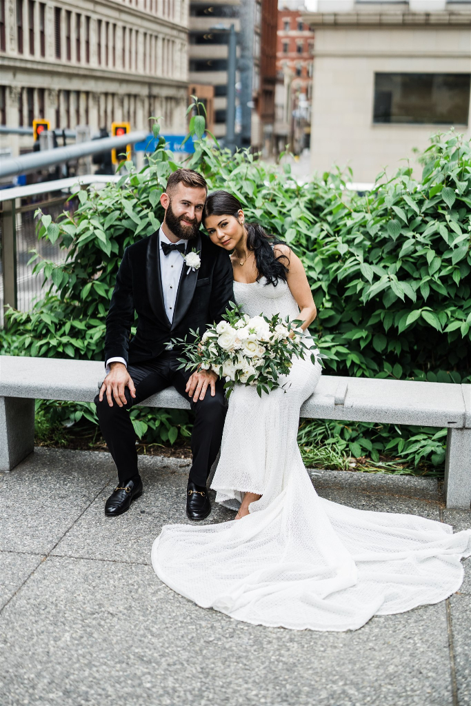 Bride and groom sit on a bench together, cuddled and smiling