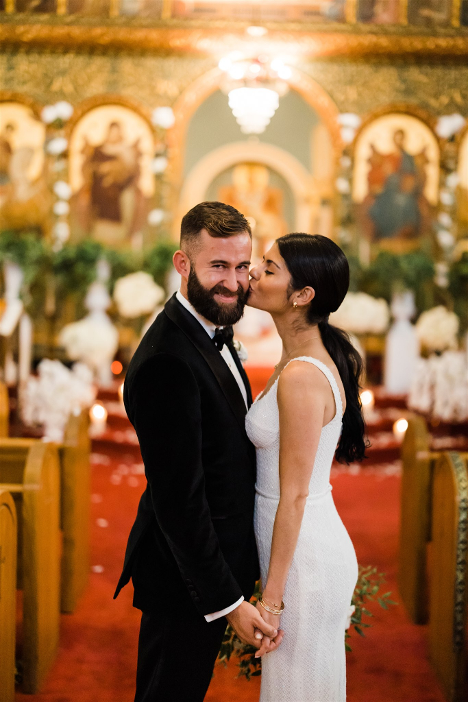 Groom smiles as bride kisses his cheek in the church