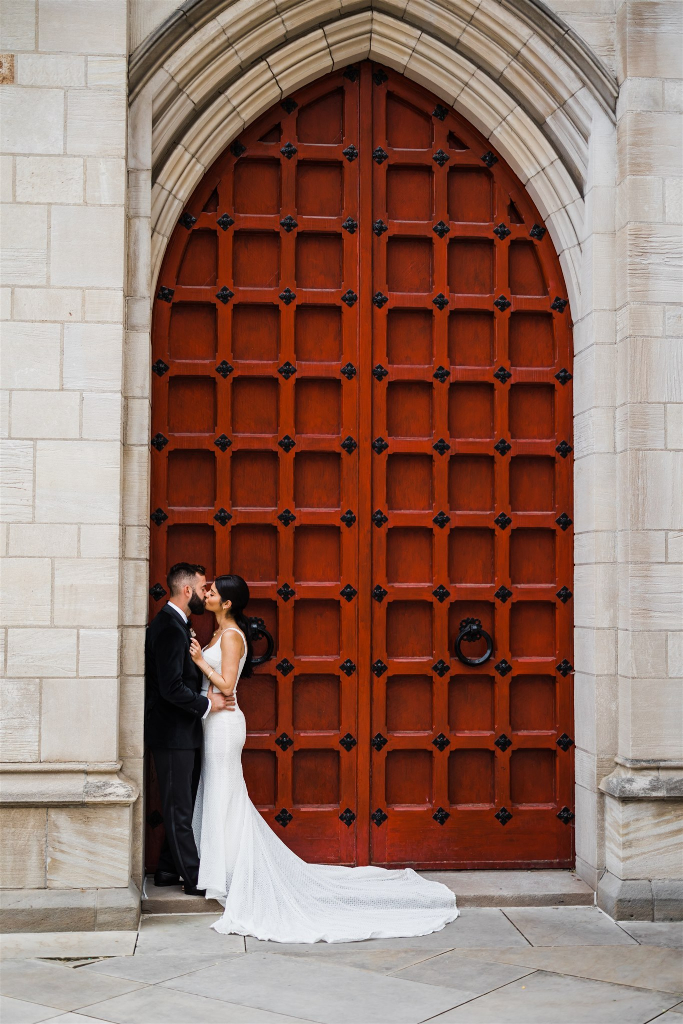 Bride and groom kiss in the doorway of a red church door