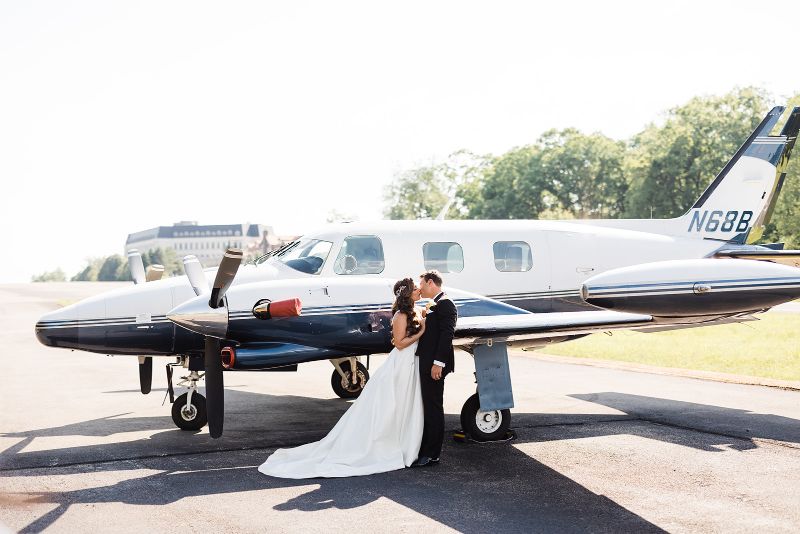 Bride and groom pose and kiss in front of small airplane