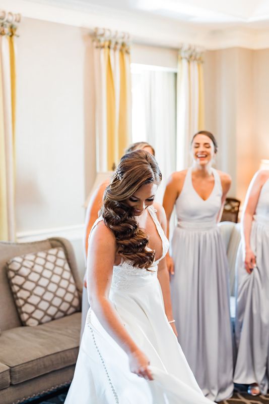 Bride smiles and shows her dress off to her bridesmaids