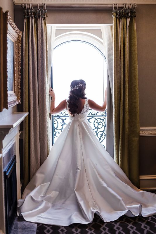 Bride looks out the window and showcases the back of her wedding gown