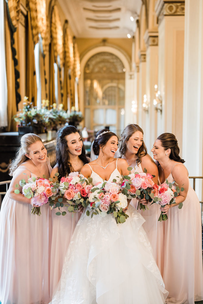 Bride smiles and laughs with her bridesmaids in the lobby of the Omni William Penn hotel