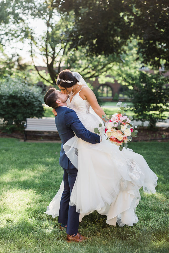 Bride and groom kiss as he lifts her up and embraces her