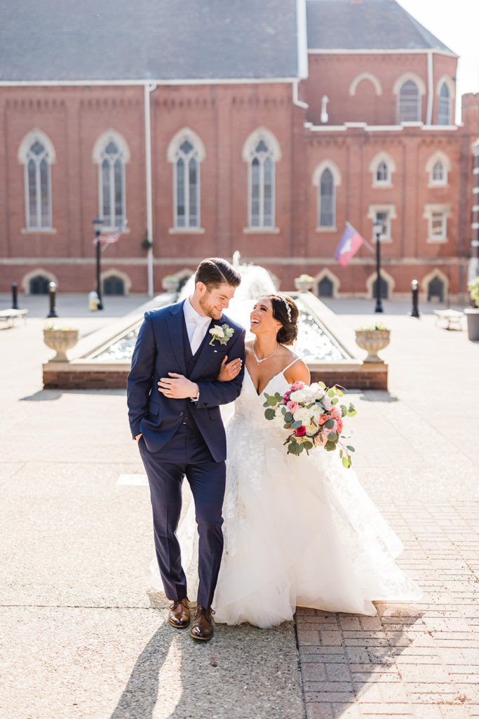 Bride and groom laugh and walk together on Duquesne University's campus