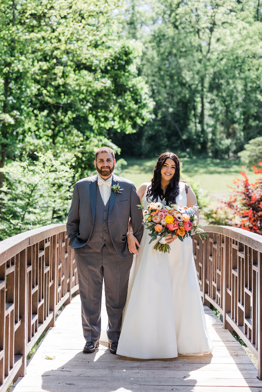 Bride and groom smile and stand on the waterlily garden bridge at their vibrant Pittsburgh Botanic Garden wedding