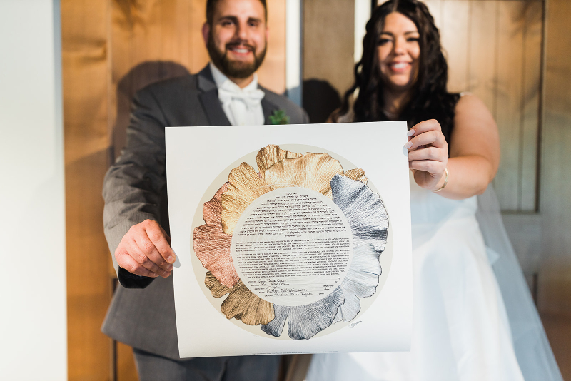 Bride and groom smile and showcase their gold and silver wedding ketubah