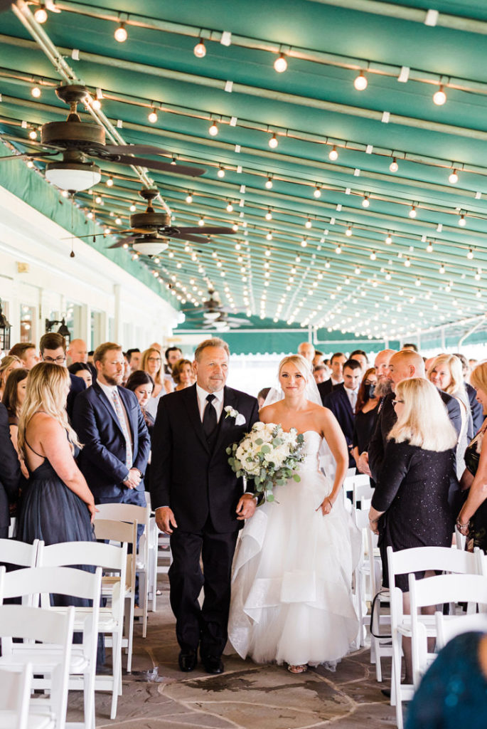 Bride walks down the outdoor aisle at Oakmont Country Club Wedding accompanied by her father