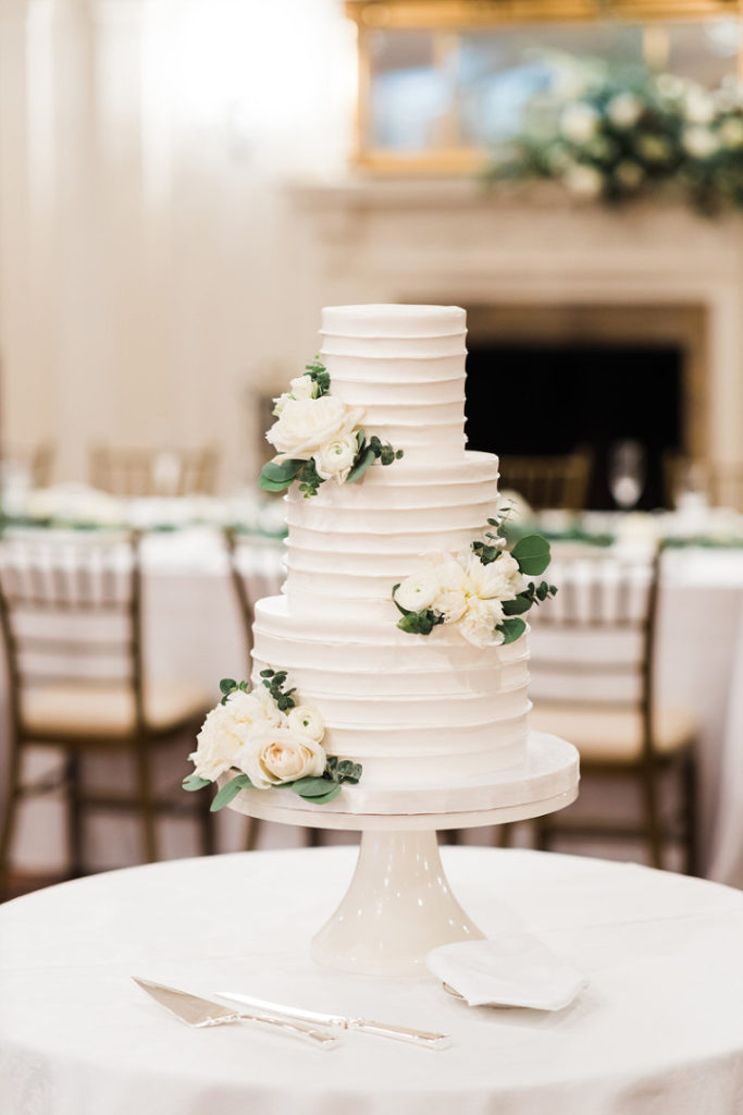All white wedding cake decorated with roses and greenery