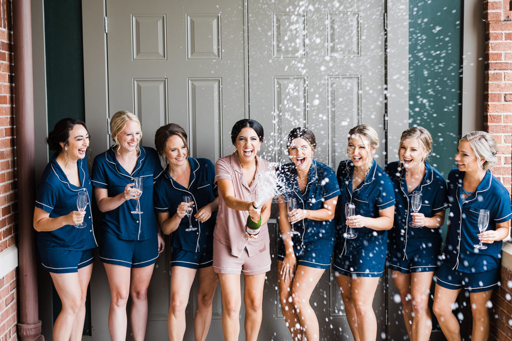 Bride pops a champagne bottle with bridesmaids standing next to her