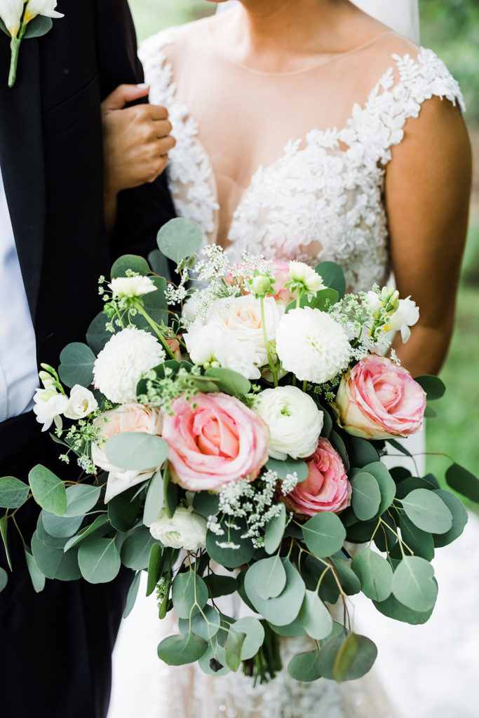 Close up photo of green, pink and white wedding bouquet in brides hands