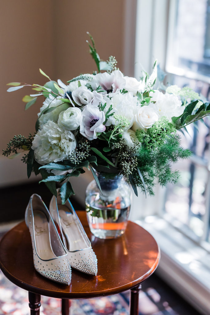 Brides shoes sitting on table next to white and green floral arrangement