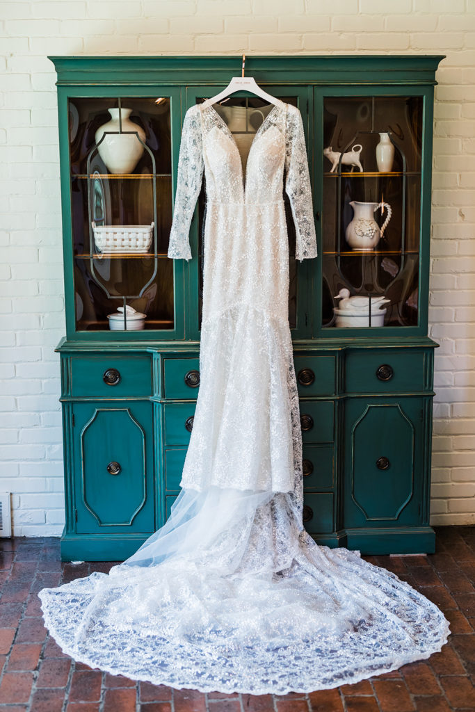 Brides dress hangs on hunter green china closet.