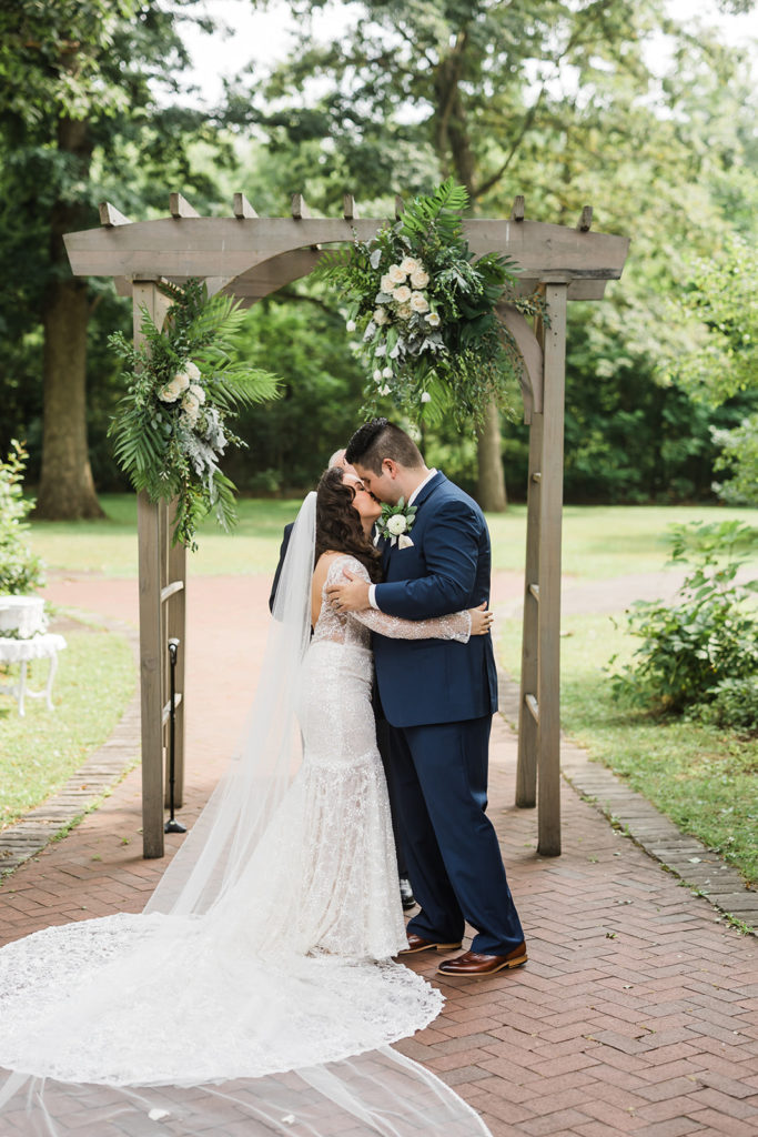 Bride and groom share first kiss under the archway at Succop Nature Park