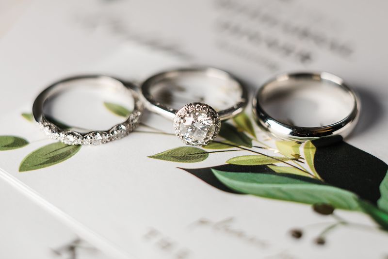 White gold wedding rings laying on greenery and invitation suite