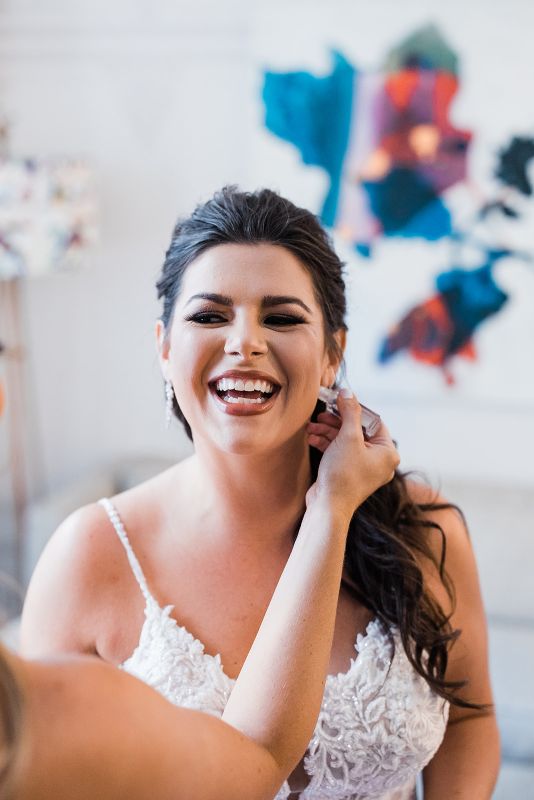 Bride smiles and laughs as her hair and makeup is finalized