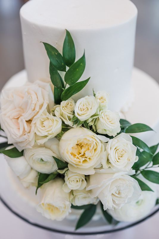 All white Oakmont Bakery wedding cake decorated with white roses and greenery