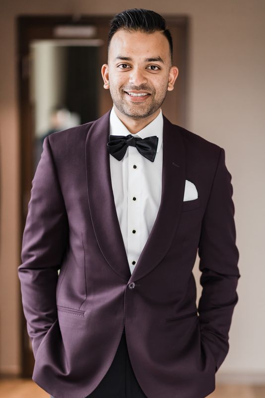 groom smiles into the camera wearing a purple suit coat