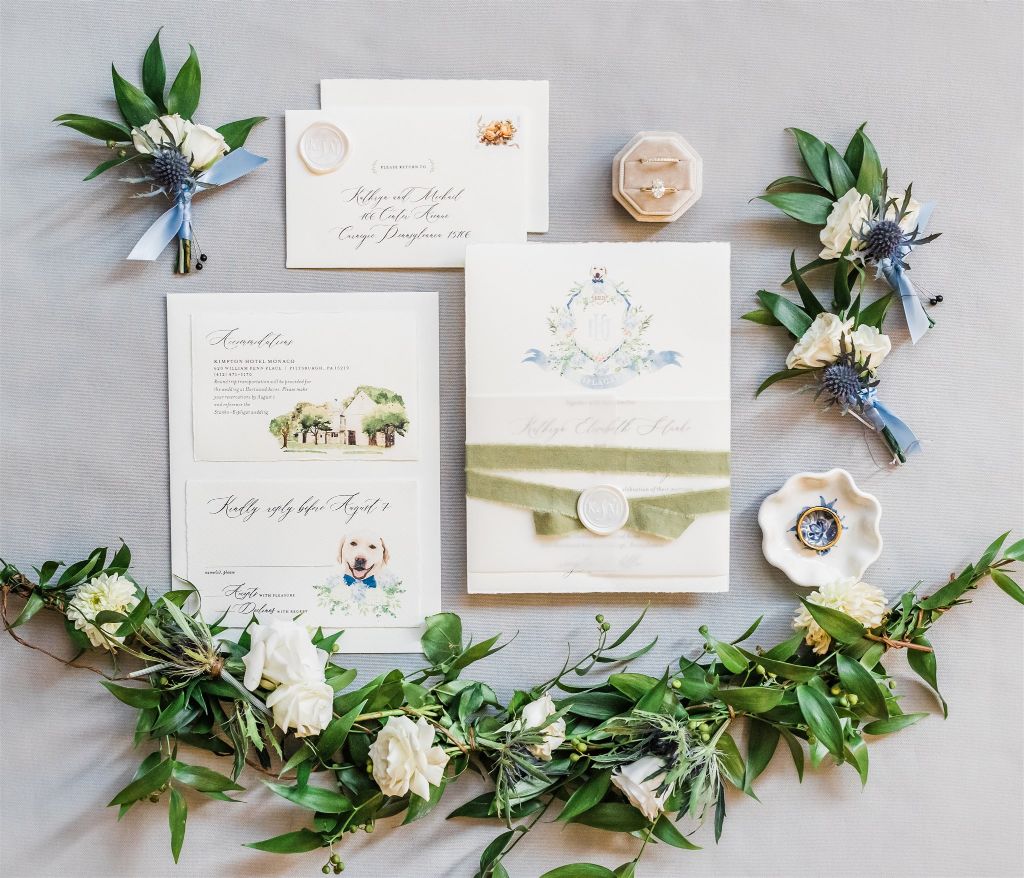 Ivory, light blue and green flat lay with stationery, rings and boutonnieres