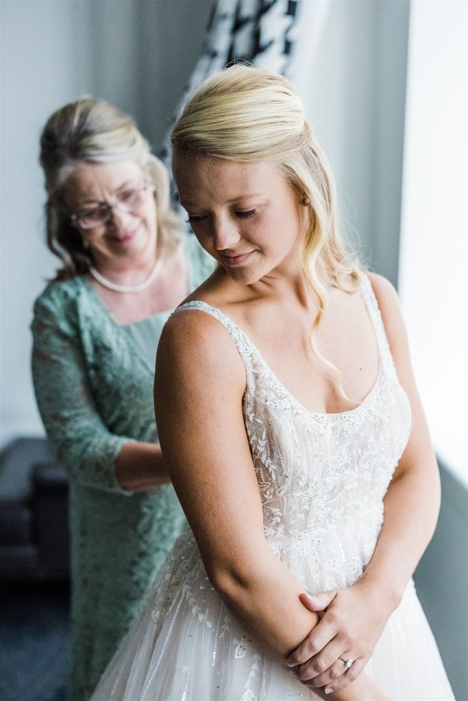 Mother of the bride smiles as she fastens the brides dress