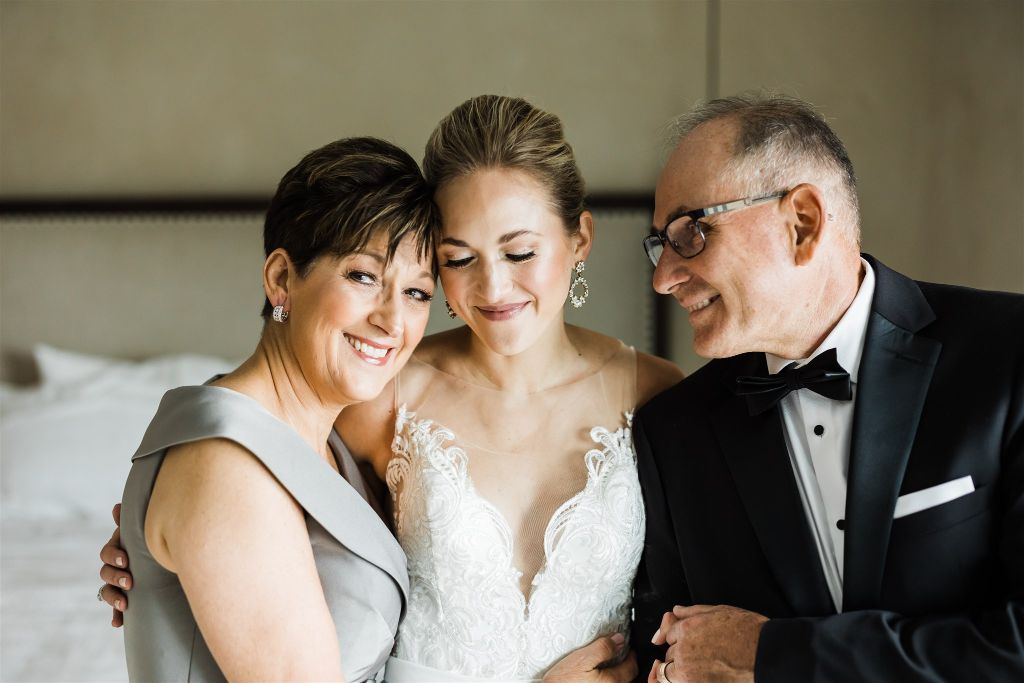 Bride and her parents smile together and embrace