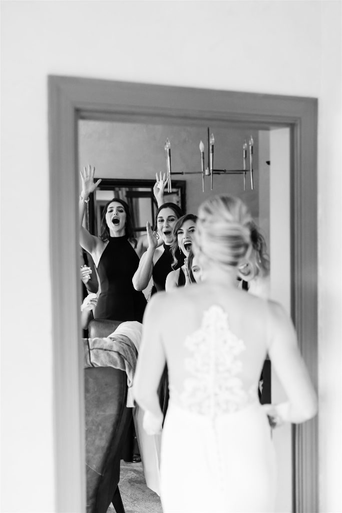Bride shows her bridesmaids her gown for the first time as the react joyfully
