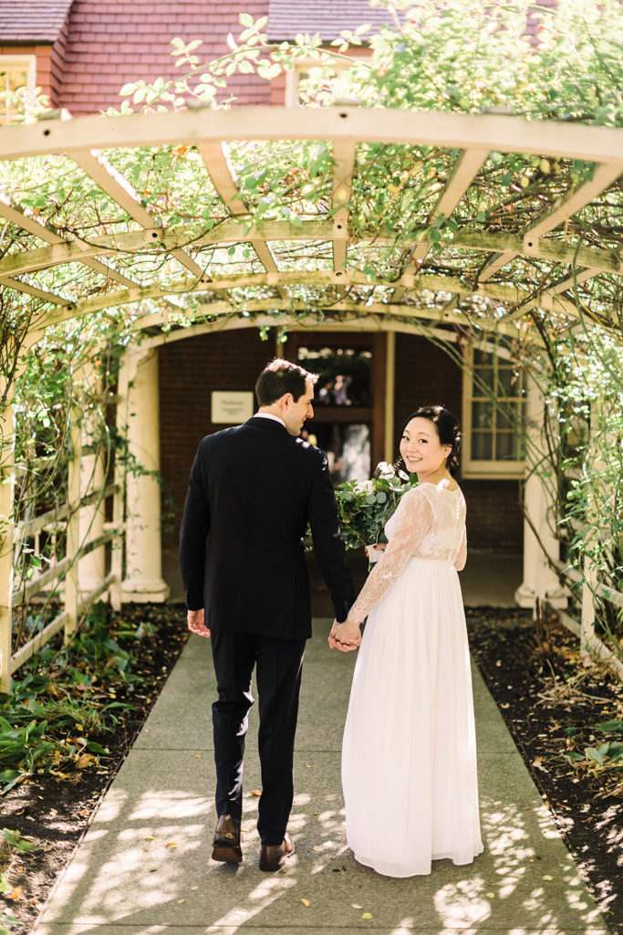 Bride and groom walk under the trellis at the Frick Clayton House