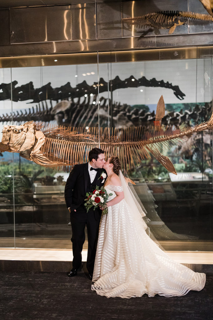 Bride and groom kiss in front of dinosaur bones
