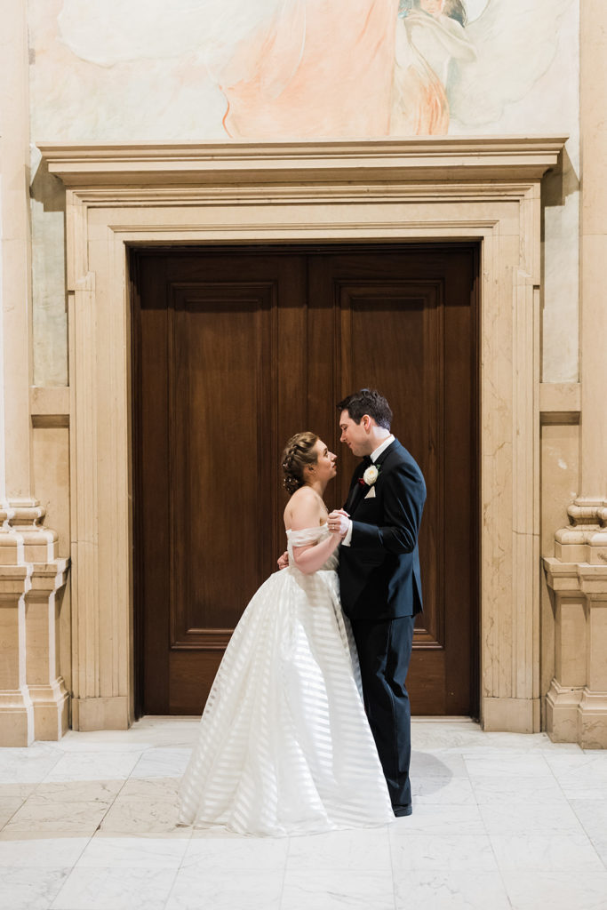 bride and groom embrace in front of large wooden doors at Carnegie Music Hall Foyer