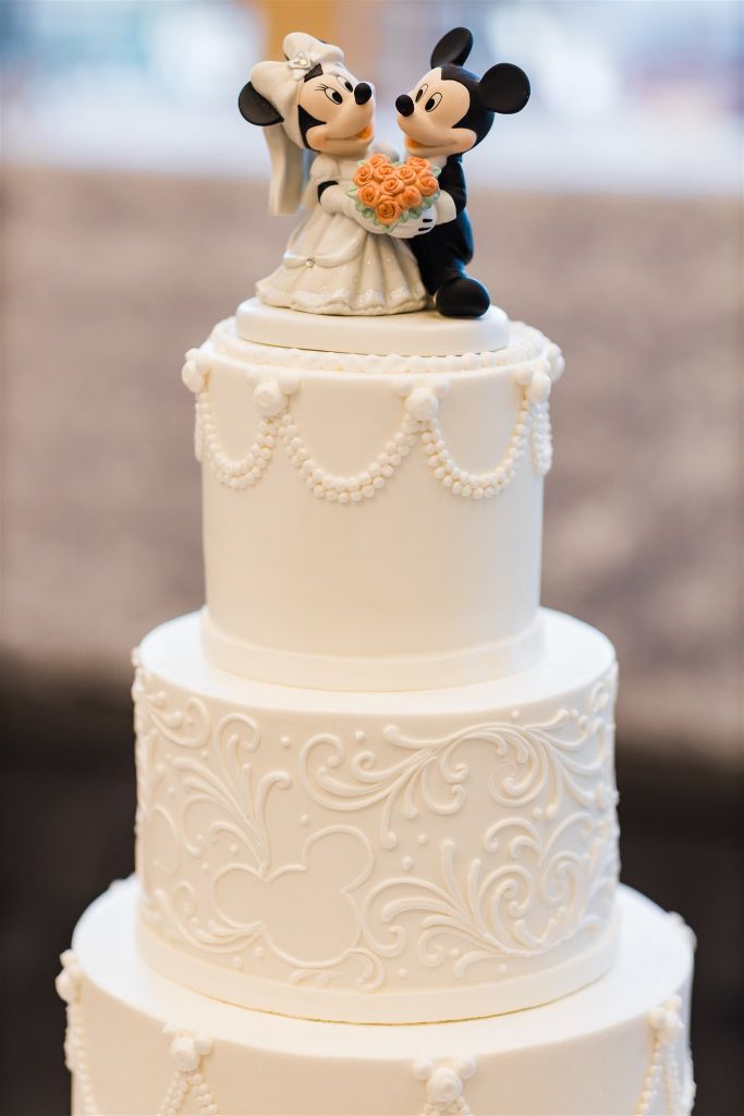 White wedding cake topped by Mickey Mouse topper