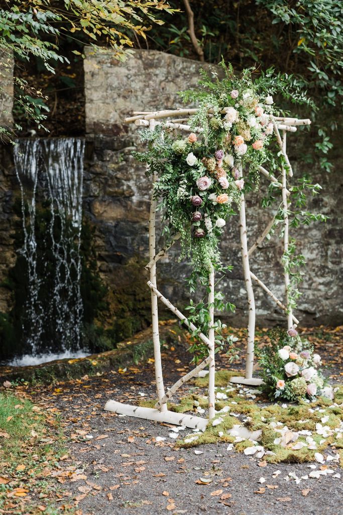 Rustic ceremony arch made of wood branches decorated with roses and greenery