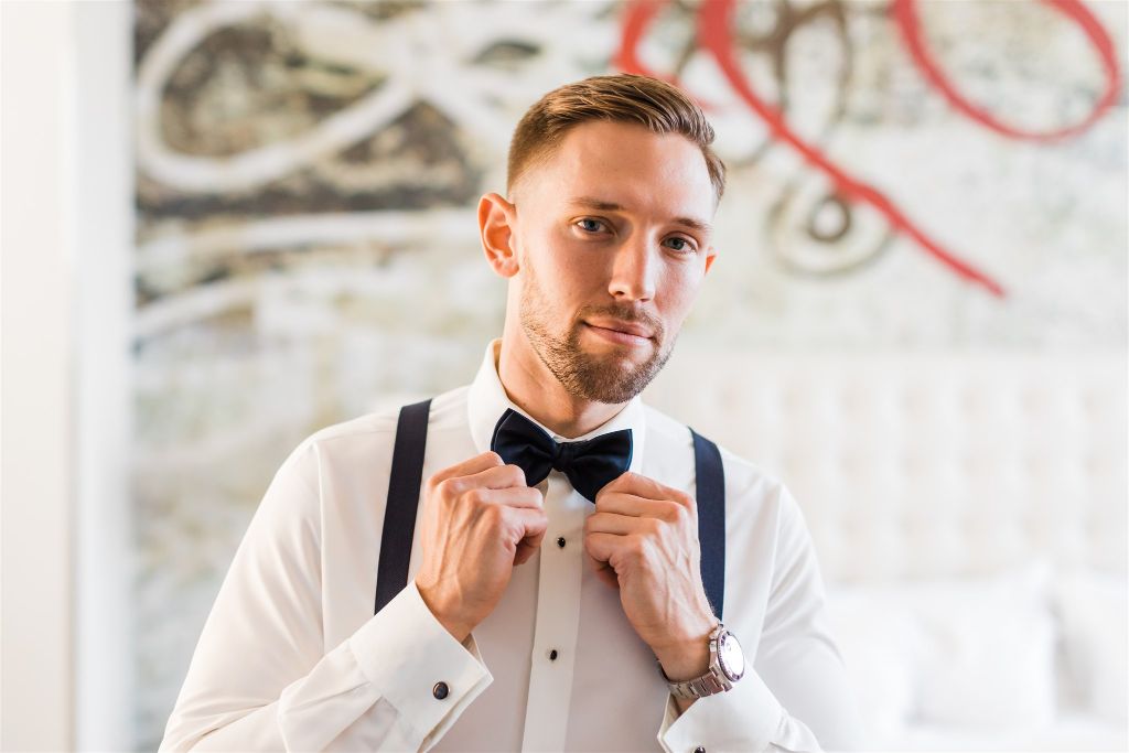 Groom looks into the camera and adjusts his bowtie