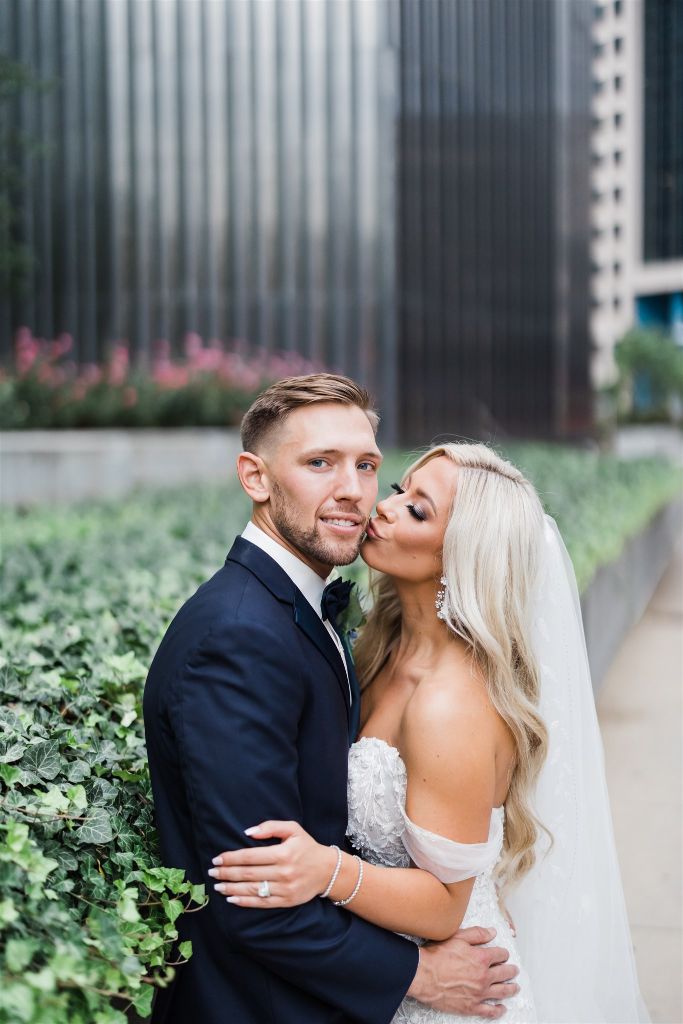 Bride kisses grooms cheek as he smiles into the camera