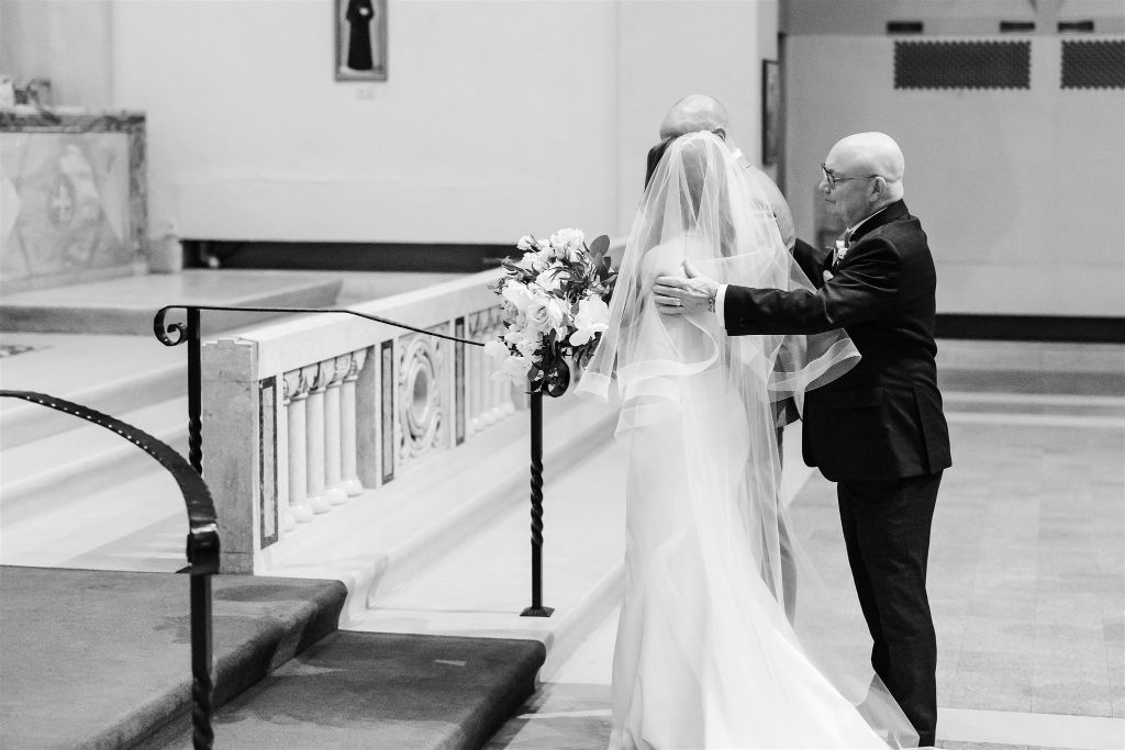Father of the bride embraces bride and groom at the end of the aisle
