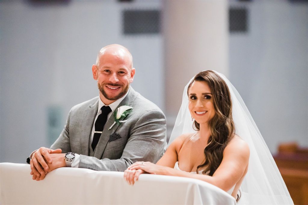 Bride and groom smile as they kneel together during wedding ceremony
