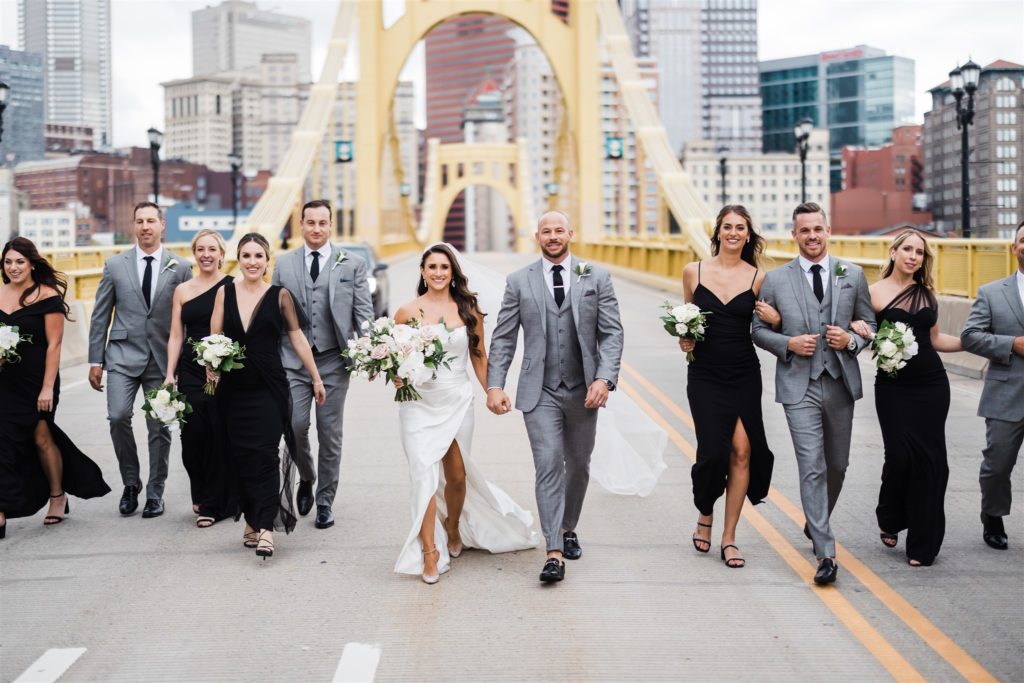 Bride and groom walk together with bridal party across the Roberto Clemente bridge