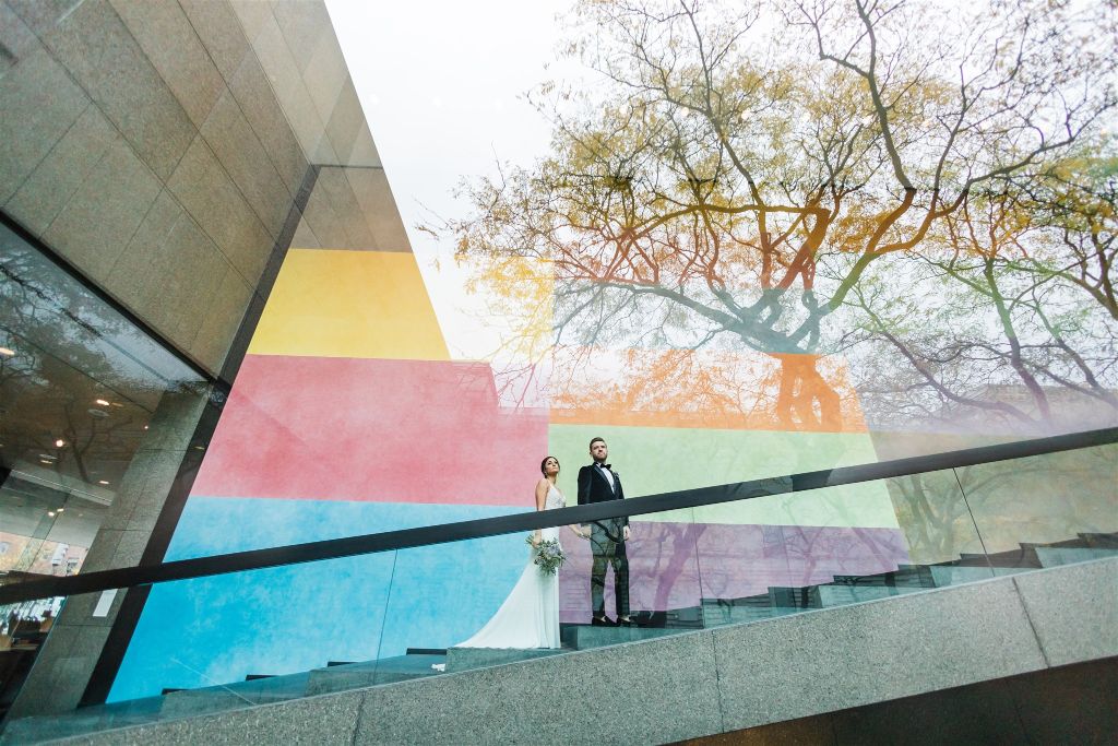 Bride and groom pose on steps in front of colorful wall at Carnegie Museum