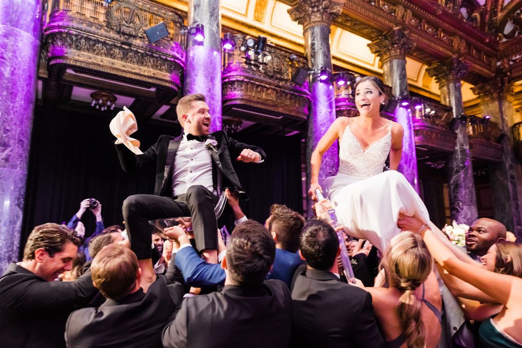 Bride and groom are lifted up in chairs during reception celebration at Jewish wedding reception at the Carnegie museum